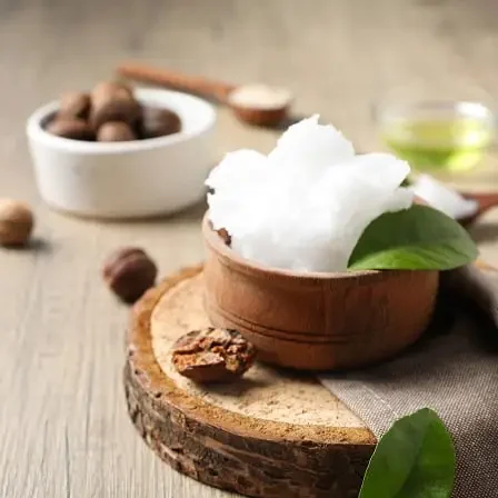 Bodegón con manteca de karité en un cuenco de madera y nueces de karité, representando su textura ideal para nutrir y suavizar la piel.