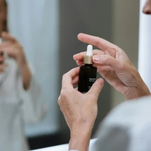 Mujer de 55 años leyendo la etiqueta de una crema facial FEBS ante el espejo. Cosmética honesta y sin tóxicos para pieles maduras que exigen resultados reales.